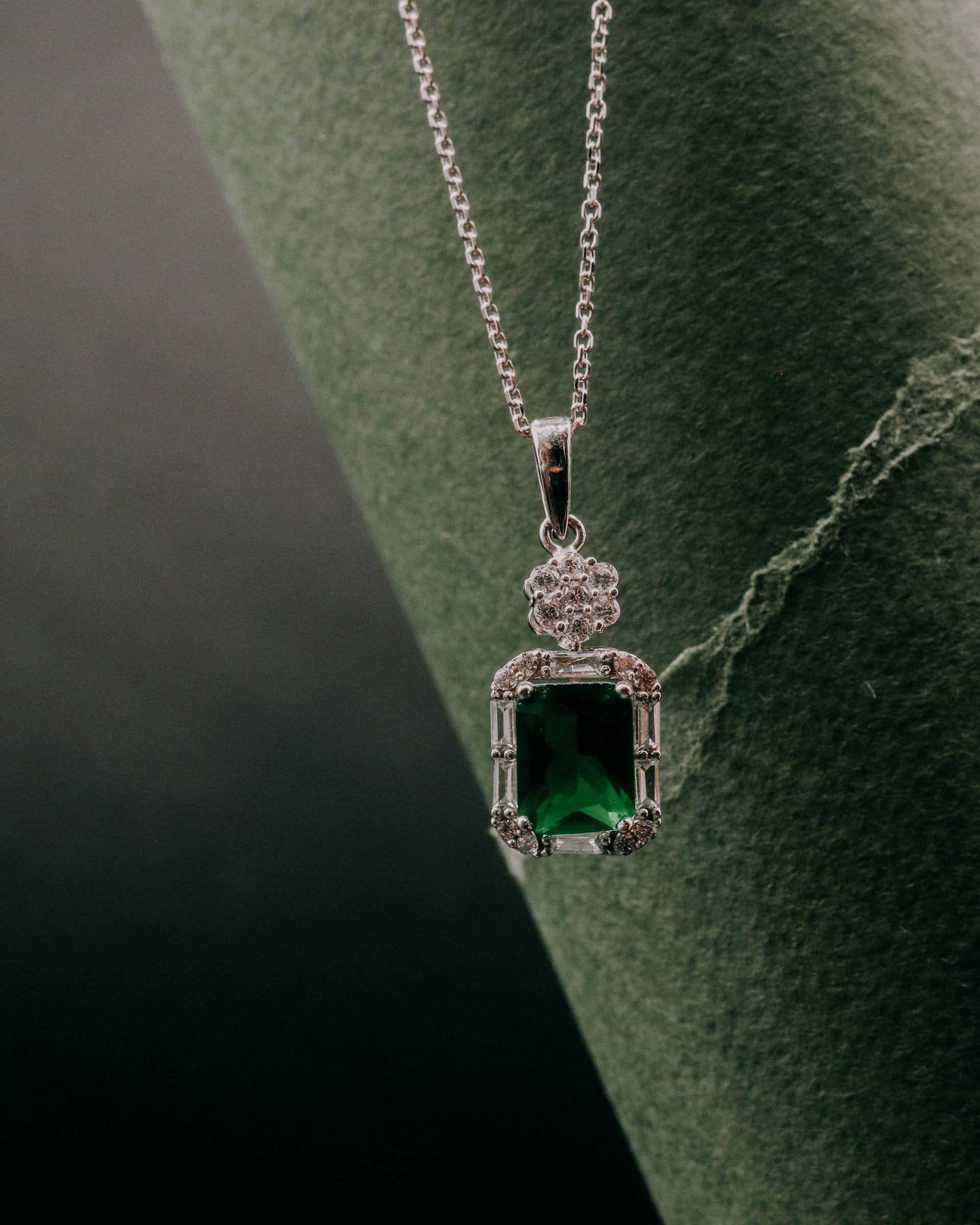 Rectangular emerald pendant in a silver-toned halo on a fine chain.